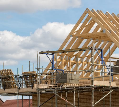 Construction industry. Timber framework of house roof trusses with scaffold on a building being built on a new housing estate.